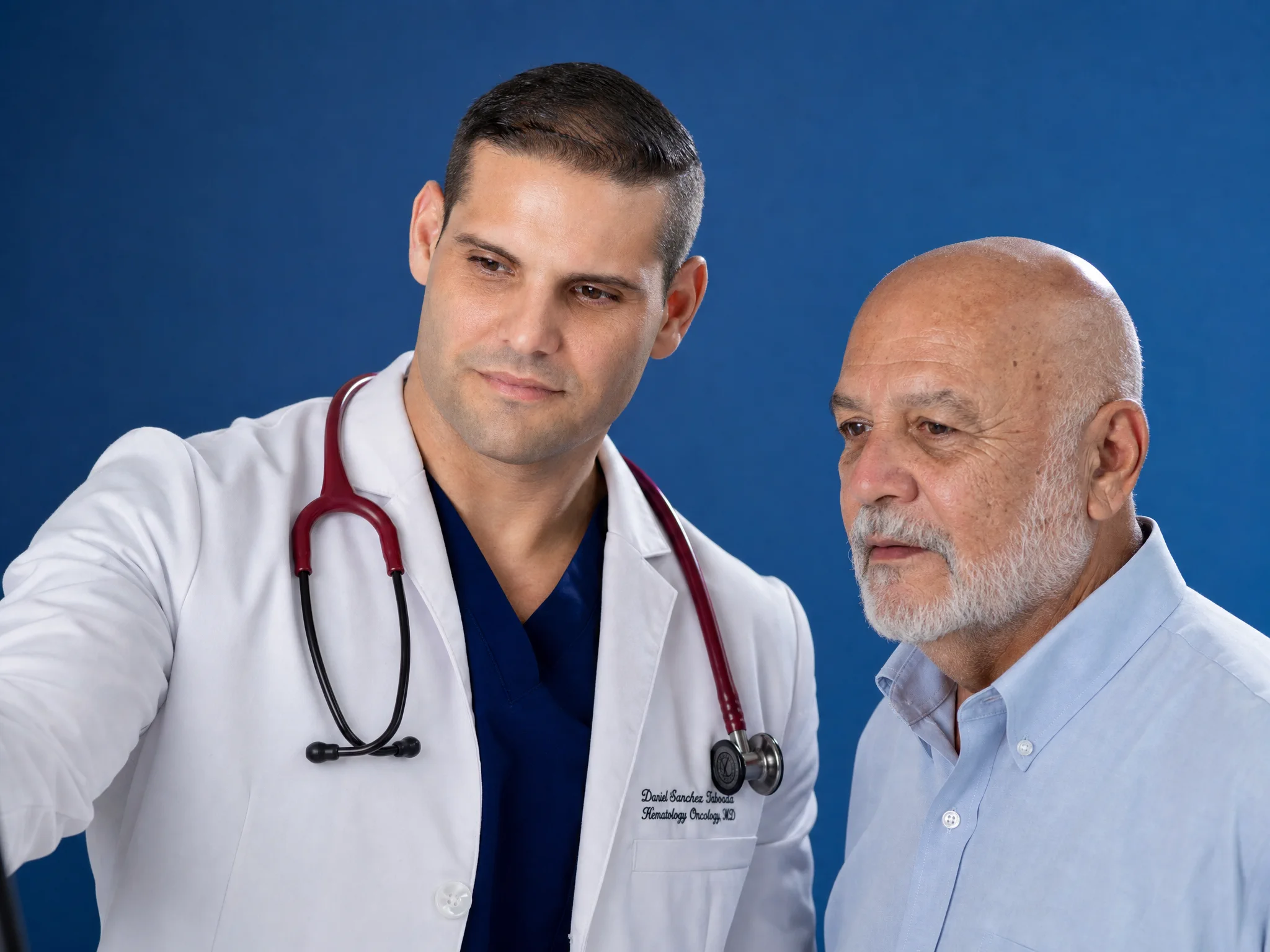 Dr. Daniel Sánchez Taboada conversa con un paciente sobre un fondo azul